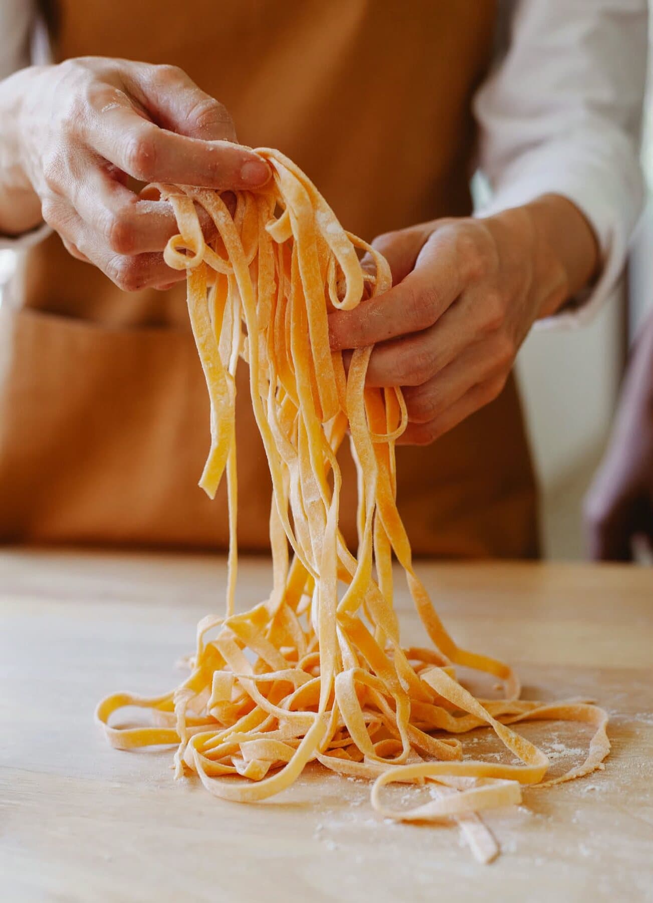 Des mains soulèvent des tagliatelle fraîches au-dessus de la table farinée