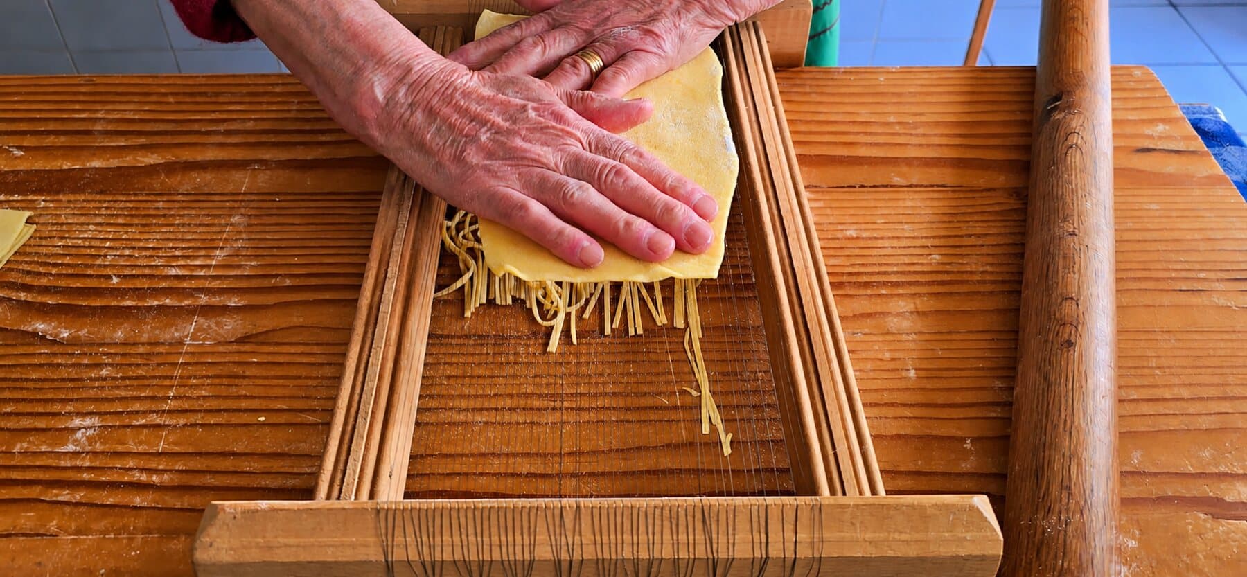 Des mains pressent la feuille de pasta sur les cordes de la chitarra