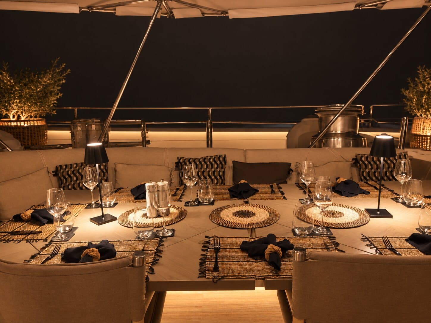 Une longue table dressée pour le dîner sur le pont d’un yacht, à la lumière des lampes