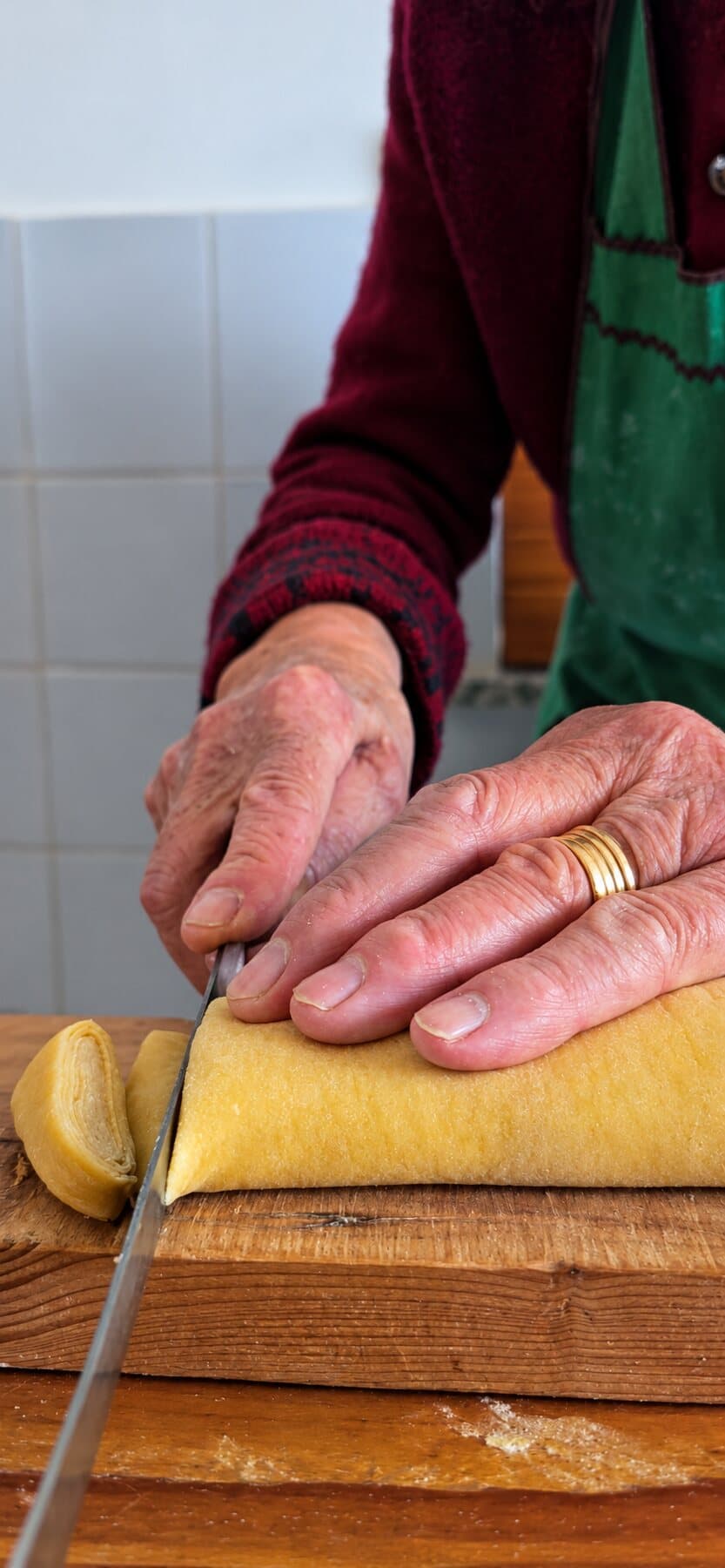 Des mains ridées coupent au couteau la feuille de pasta roulée