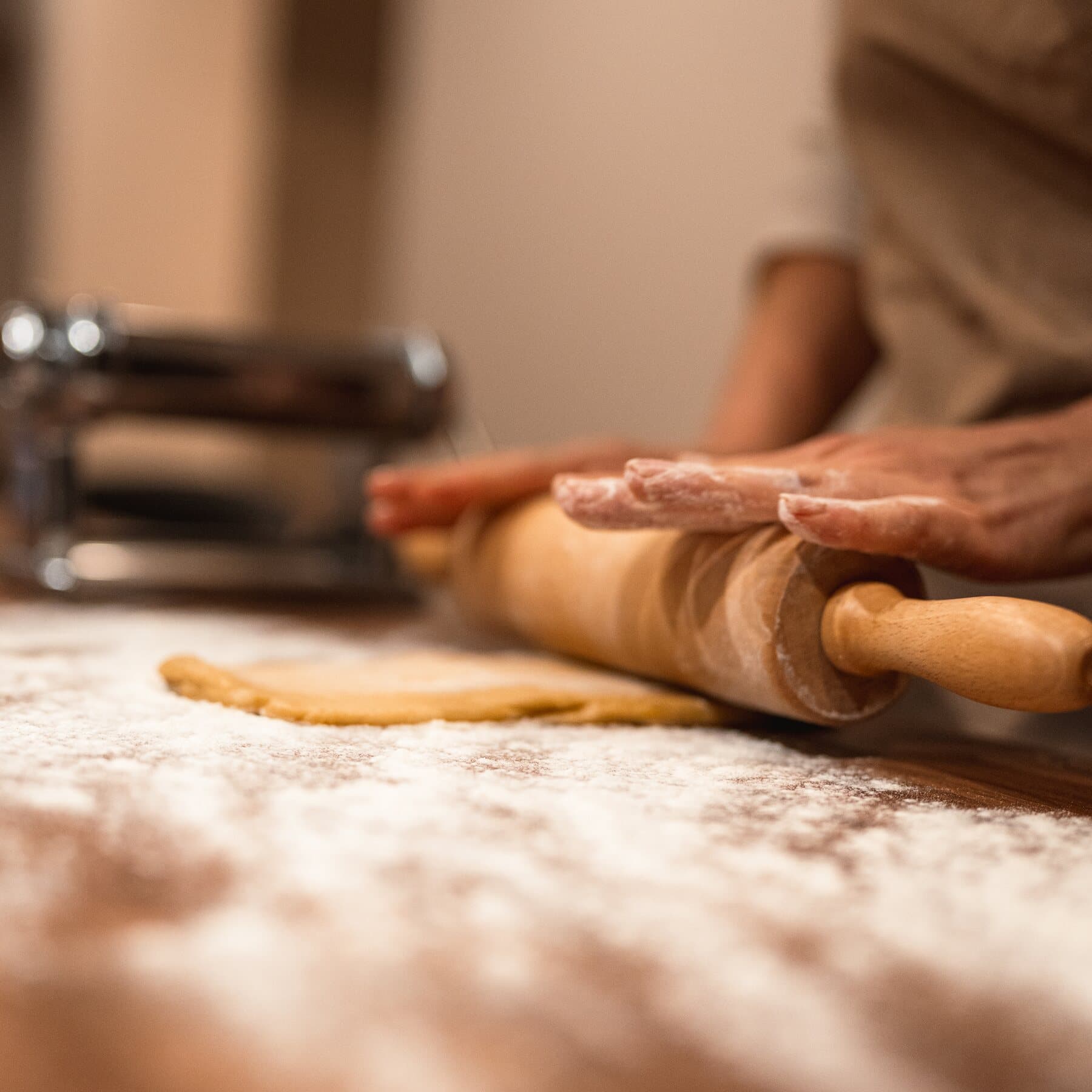 Des mains farinées abaissent la pasta au rouleau, sur la table couverte de farine
