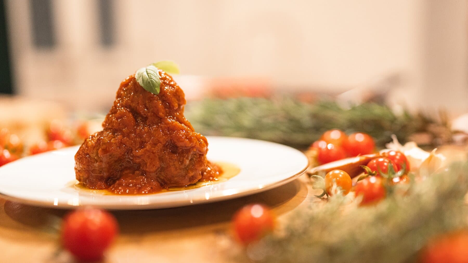 Des polpette nappées de sauce tomate, une feuille de basilic, des tomates cerises autour