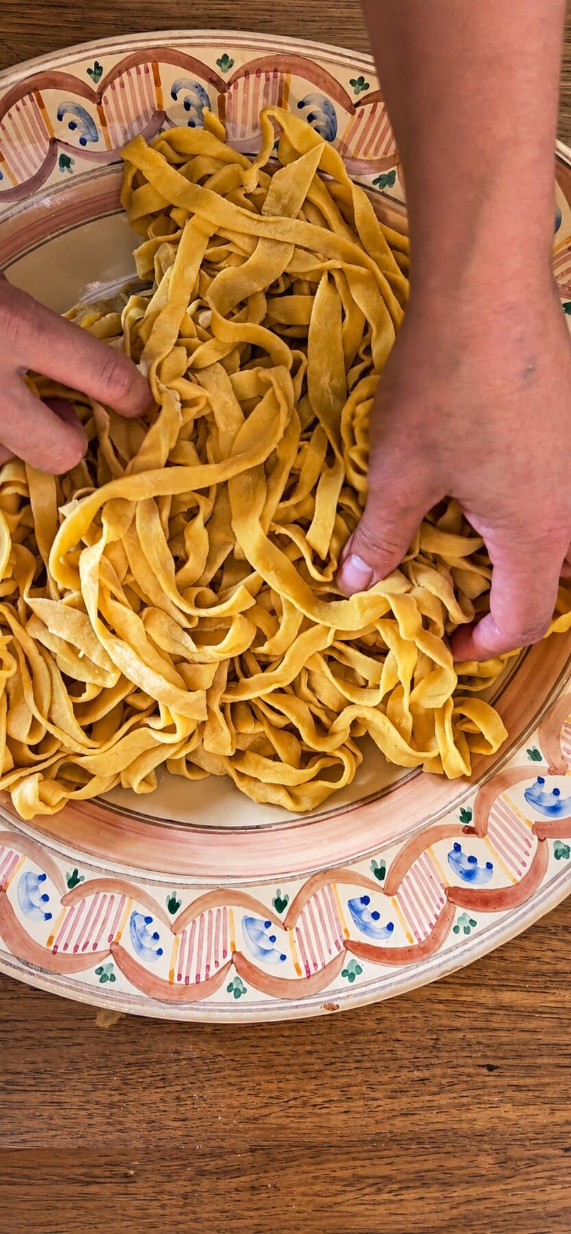 Des mains dans les tagliatelle fraîches, sur une assiette peinte à l’italienne