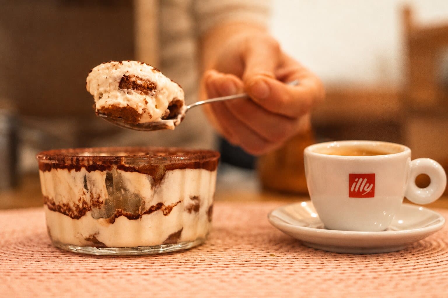 Une cuillerée de tiramisù au-dessus de sa verrine, une tasse de caffè à côté