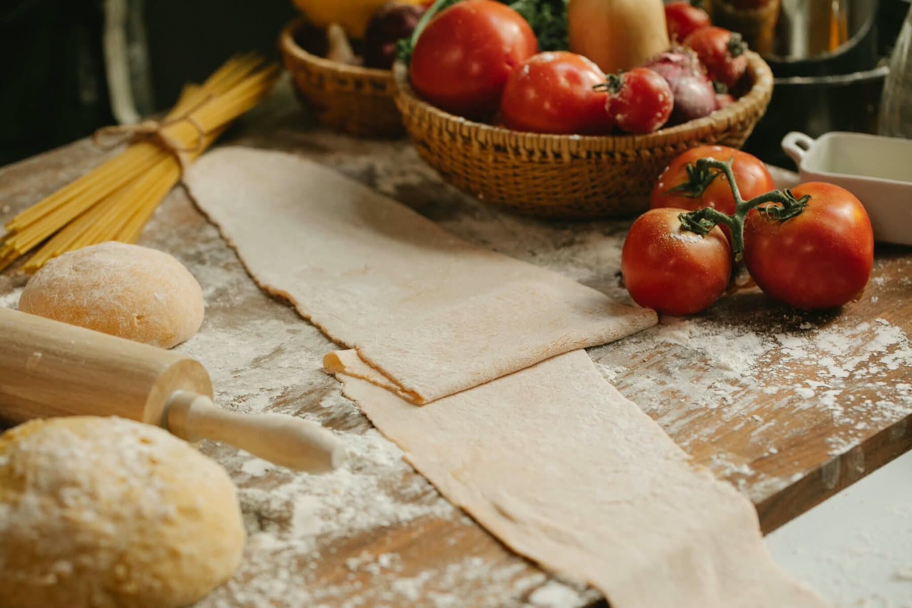 Des feuilles de pasta sur la table farinée, des tomates en grappe, des spaghetti et le rouleau