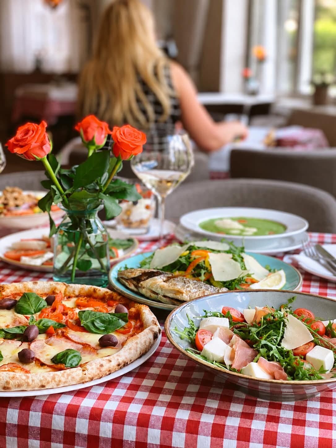 Une table à la nappe à carreaux rouges : pizza, salades, poisson grillé, roses et vin blanc