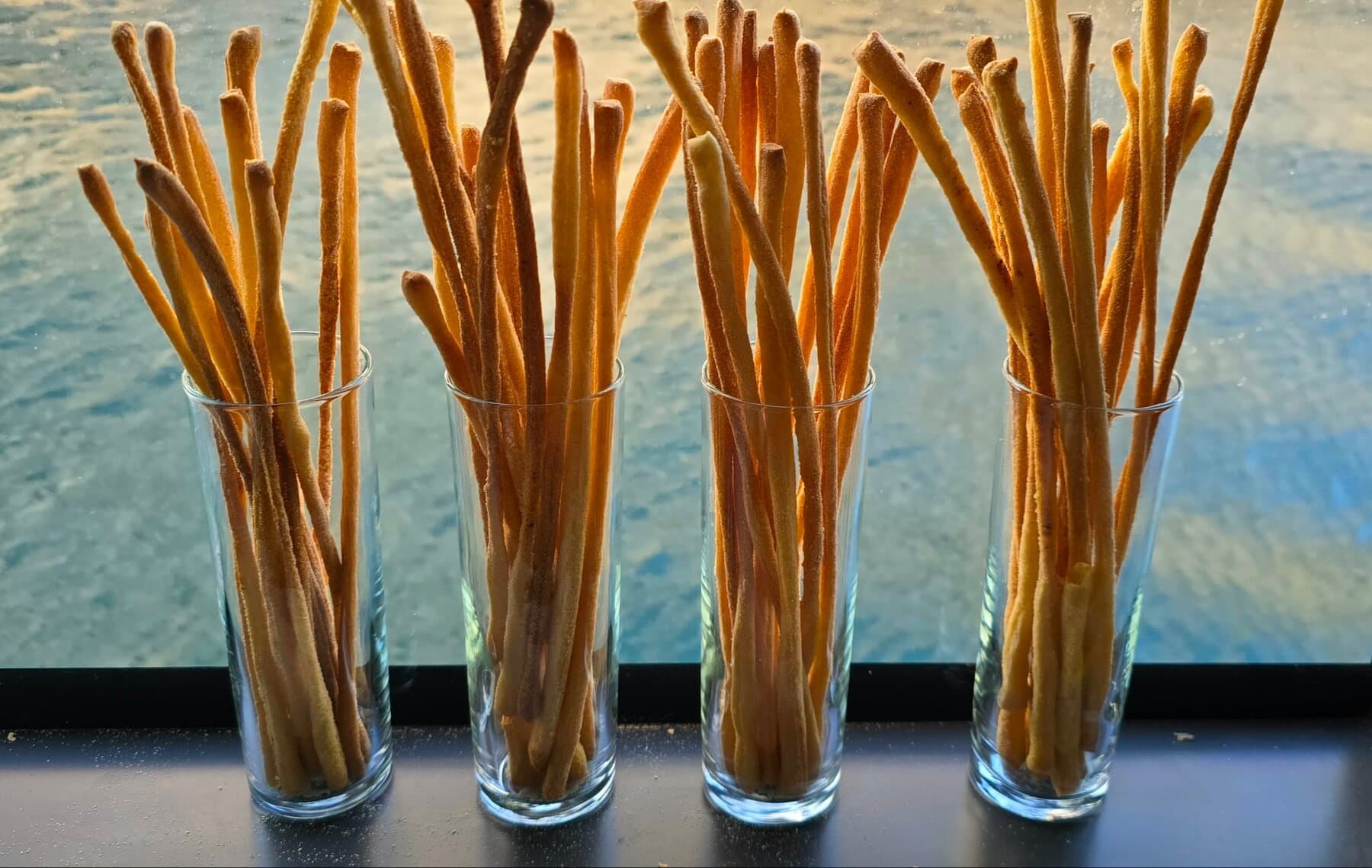 Des grissini dressés dans des verres, devant la mer