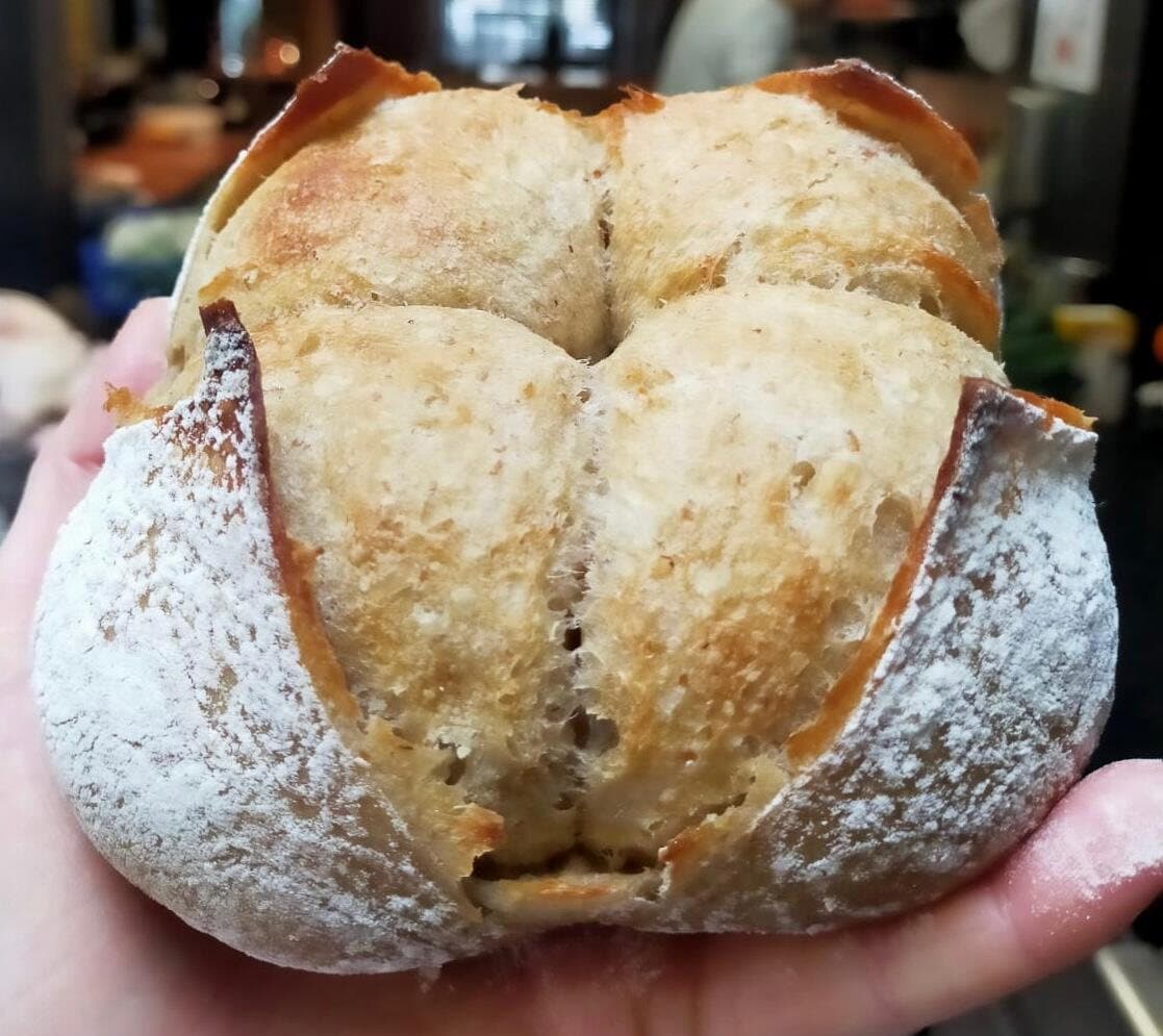 Une boule de pain au levain tenue dans la main, la croûte farinée et fendue