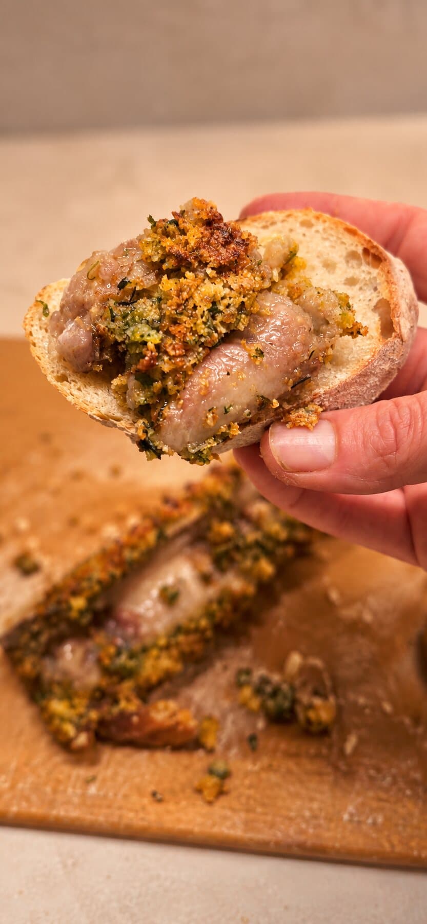 Une tranche de pain garnie de saucisse et d’une chapelure aux herbes, tenue à la main
